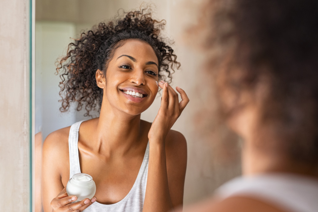 Young african woman applying moisturizer on her face.